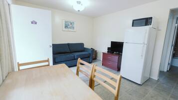 Ein kompakter Wohnbereich mit Esstisch, Stühlen, einer Couch, einem Fernseher, einem Kühlschrank und einer Mikrowelle.