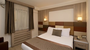 Una habitación de hotel con cama, mesitas de noche, lámpara y ventana con cortinas.