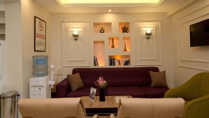 Una sala de estar con sofá, sillones, una mesa de centro, televisión y una pared decorada con objetos y un dispensador de agua.