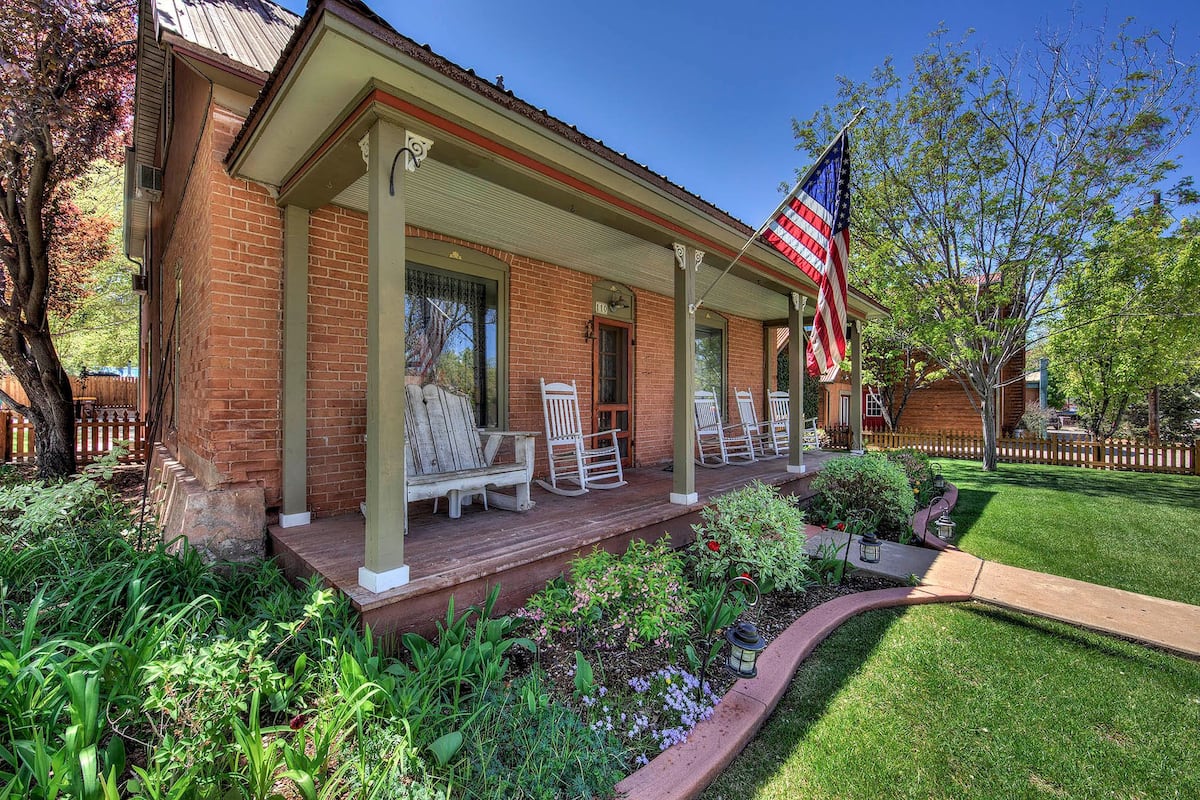 A brick house with a porch, three rocking chairs, and an American flag.