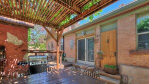 A patio area with a wooden table and chairs, a grill, and a brick wall. - Cali Cochitta Vacation Rentals (Moab)
