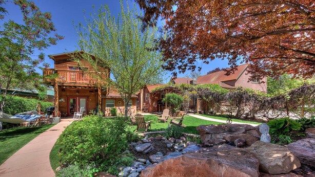A wooden cabin with a balcony, surrounded by a well-maintained garden with rocks and a small stream. - Cali Cochitta Vacation Rentals (Moab)
