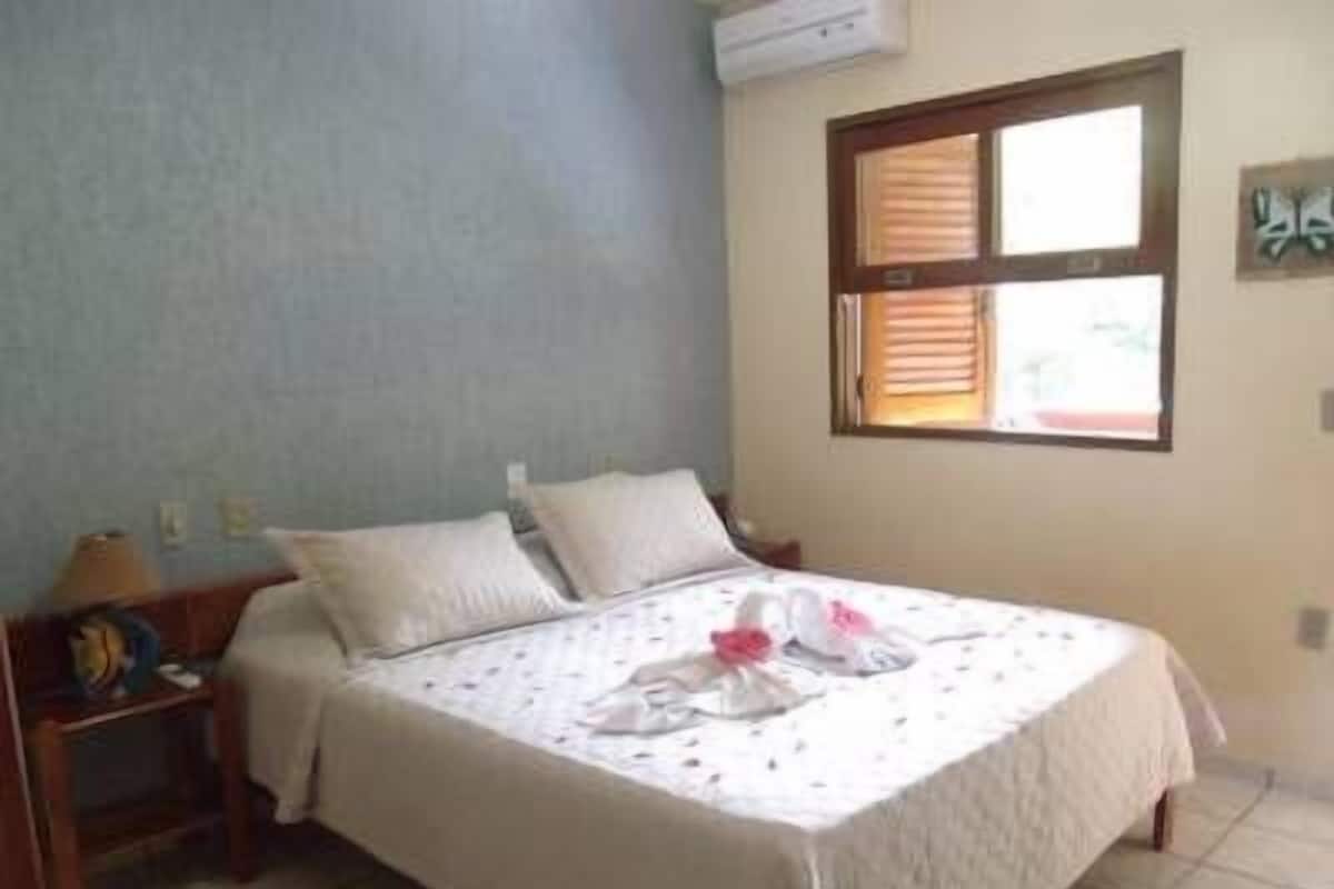 A bedroom with a bed, a nightstand, a window, and a wall-mounted air conditioner.