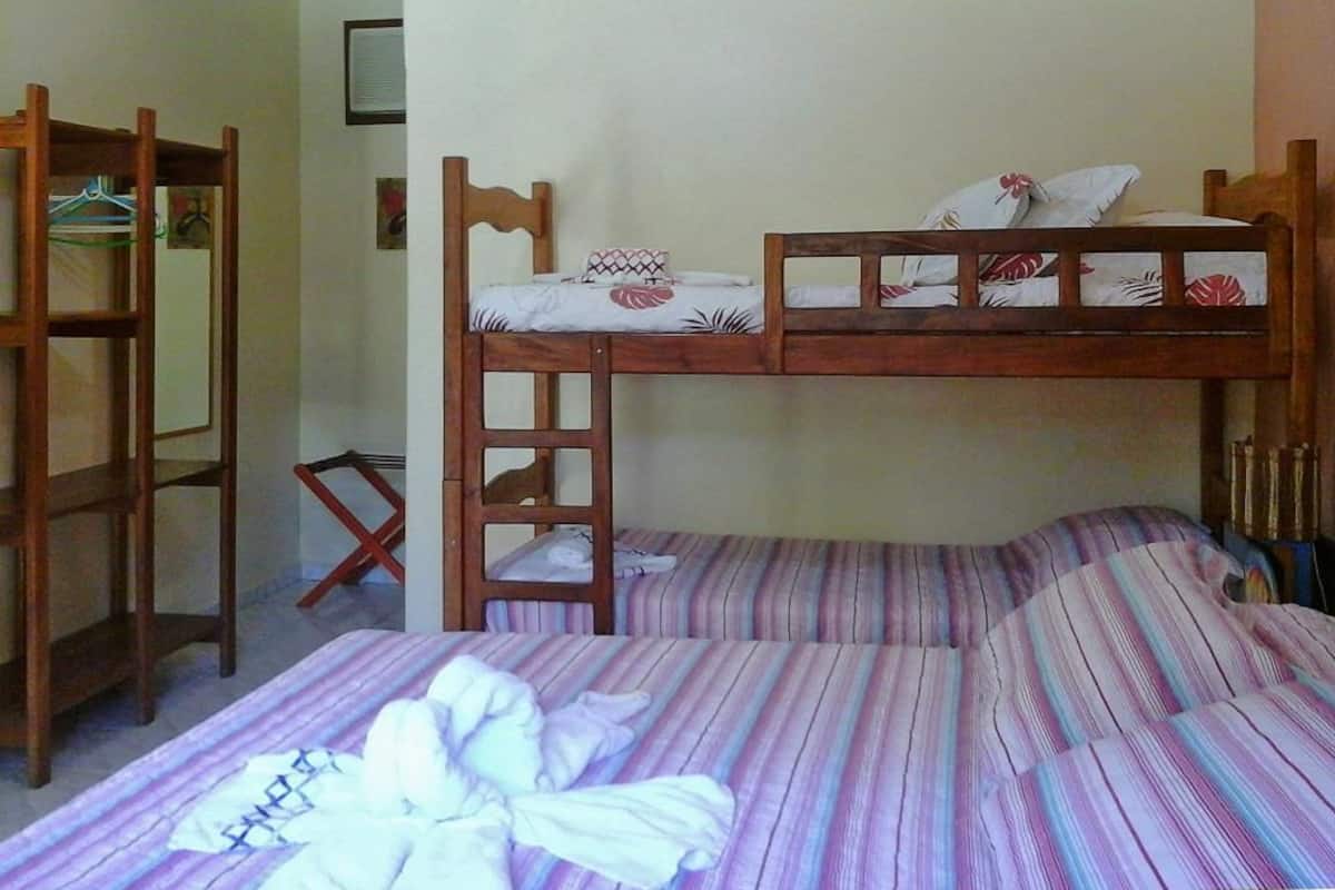 A bunk bed room with a wooden ladder, a single bed with striped bedding, and a chair.