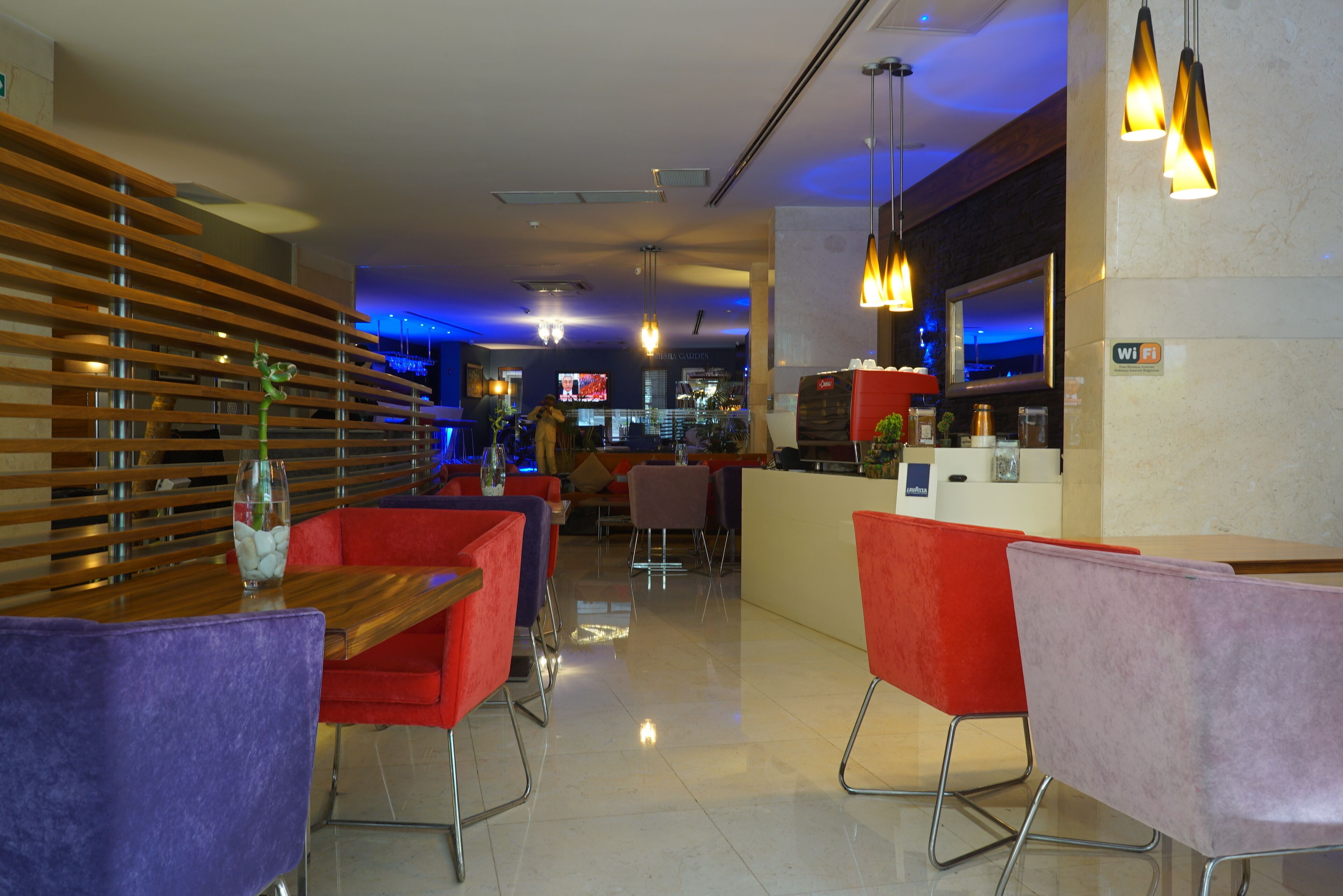 A modern hotel lobby with a bar area, red and purple seating, and a wooden slatted wall.