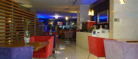 A modern hotel lobby with a bar area, red and purple seating, and a wooden slatted wall.