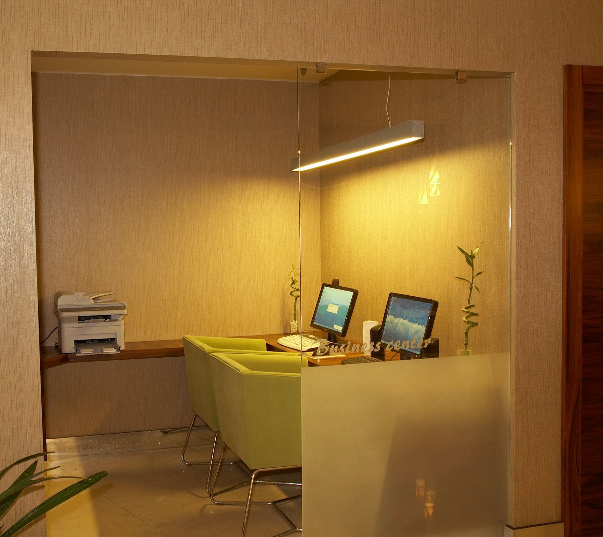 A reception desk with two computer monitors, a printer, and a green chair.