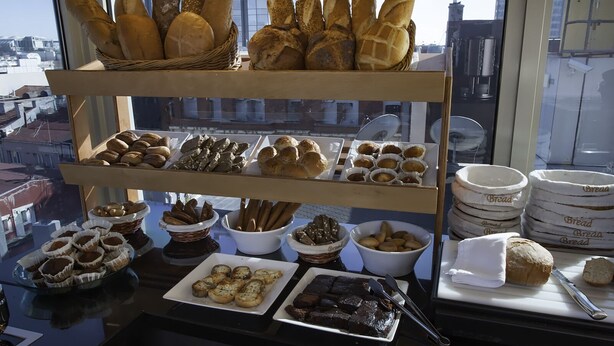 A variety of breads and pastries displayed on shelves and tables, with a view of buildings outside. - Troya Hotel (Istanbul)