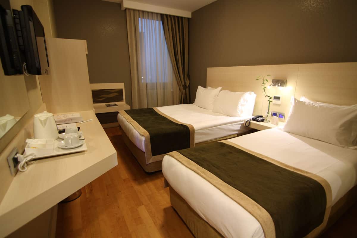 Une chambre d’hôtel avec deux lits, un bureau avec une tasse et une assiette, et une fenêtre avec des rideaux.