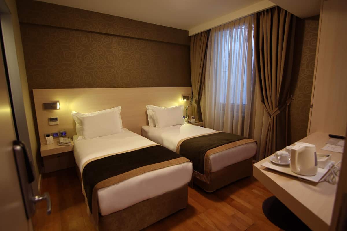 Une chambre d’hôtel avec deux lits, un bureau et une fenêtre avec des rideaux.