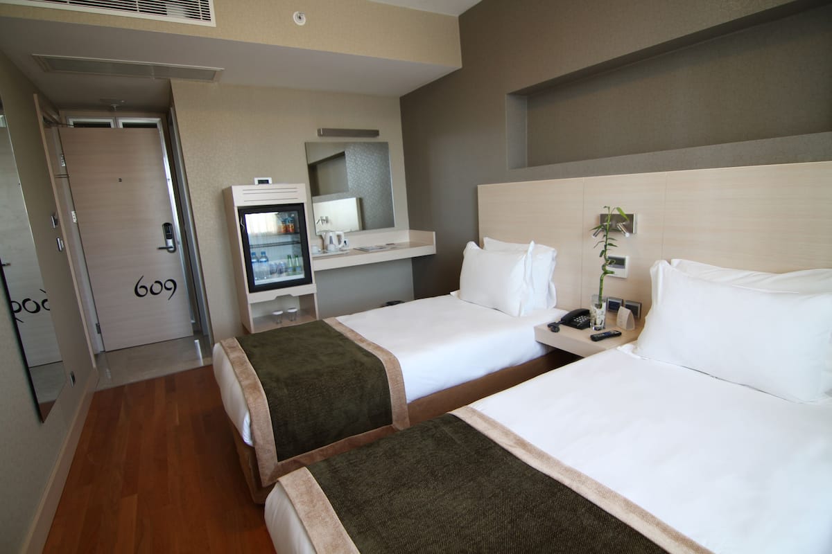 Une chambre d’hôtel avec deux lits, un bureau avec un ordinateur, un miroir et une porte portant le numéro 609.