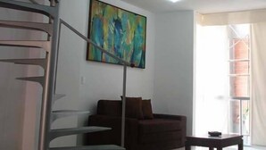 A modern living room with a spiral staircase, a large abstract painting, a brown sofa, and a small table. - Suites House Juanambu Apartasuites (Cali)