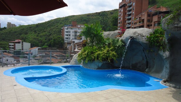 A swimming pool with a waterfall feature, surrounded by a tiled deck and greenery. - Suites House Juanambu Apartasuites (Cali)