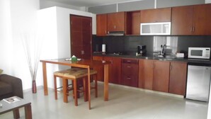 A compact kitchen with wooden cabinets, a microwave, a coffee maker, and a small dining table with chairs. - Suites House Juanambu Apartasuites (Cali)