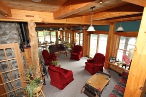 Interior acogedor de una cabaña con paredes de madera, chimenea de piedra y una zona de estar con sillas rojas y un sofá.