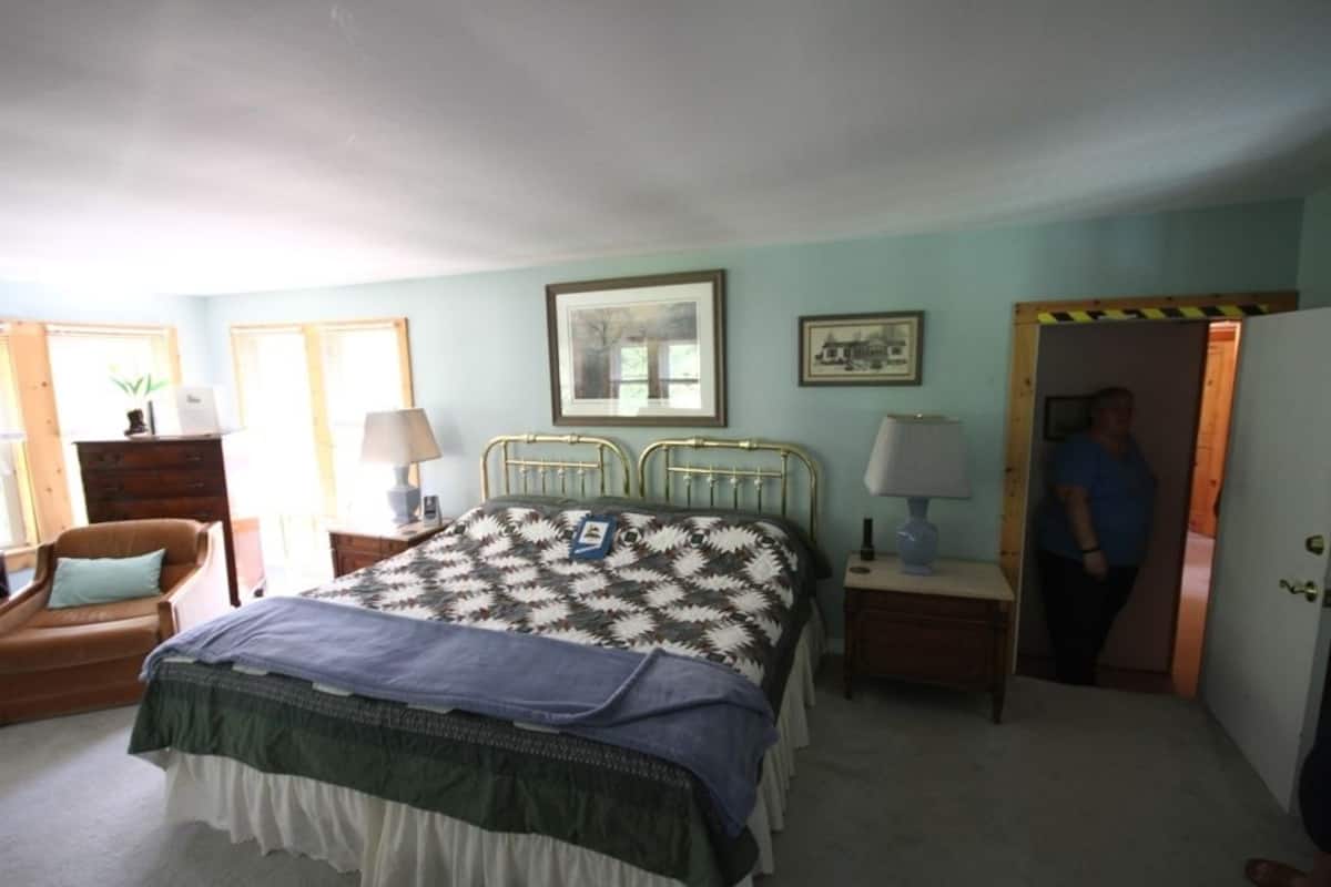 Une chambre à coucher comprenant un lit, deux tables de chevet, une chaise et une porte donnant sur une autre pièce.