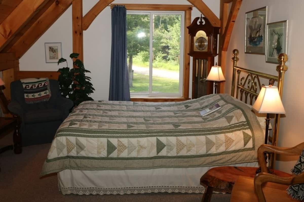 Une chambre confortable avec un grand lit, une chaise en bois, un bureau et une fenêtre donnant sur un paysage verdoyant.