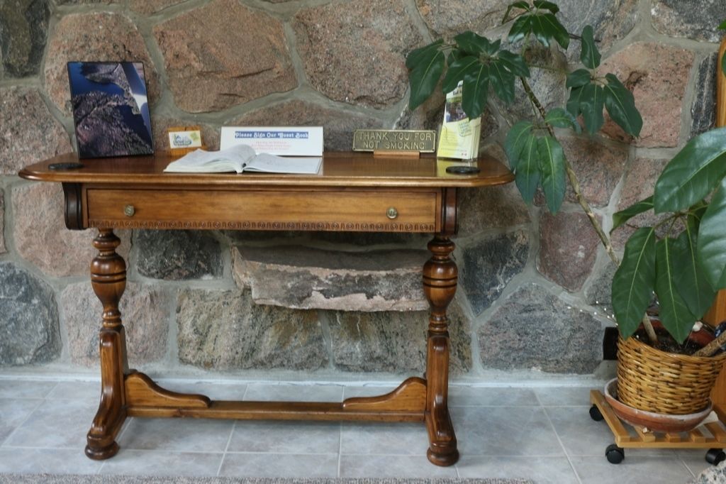 A wooden table with a stone wall background, a book, a sign, and a potted plant.