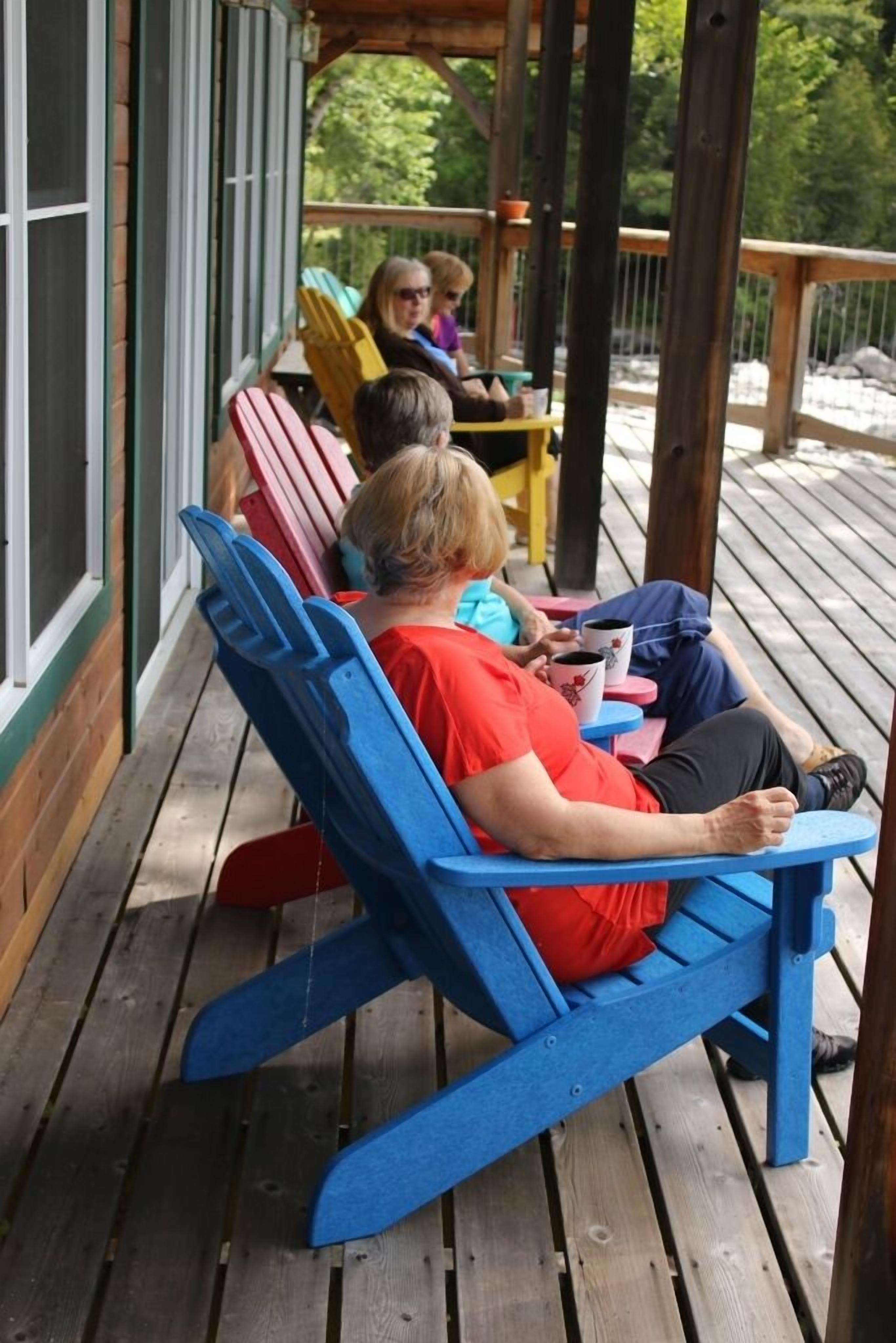 A wooden deck with blue and red Adirondack chairs.