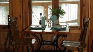 Una mesa de comedor de madera con dos sillas, una planta en maceta y un ventanal con vistas a un lago y árboles.