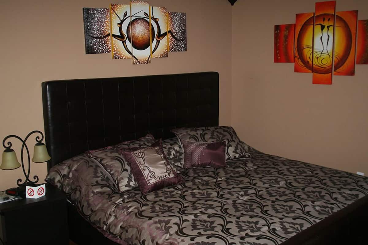 A bedroom with a large bed, a headboard, and two wall-mounted lamps.