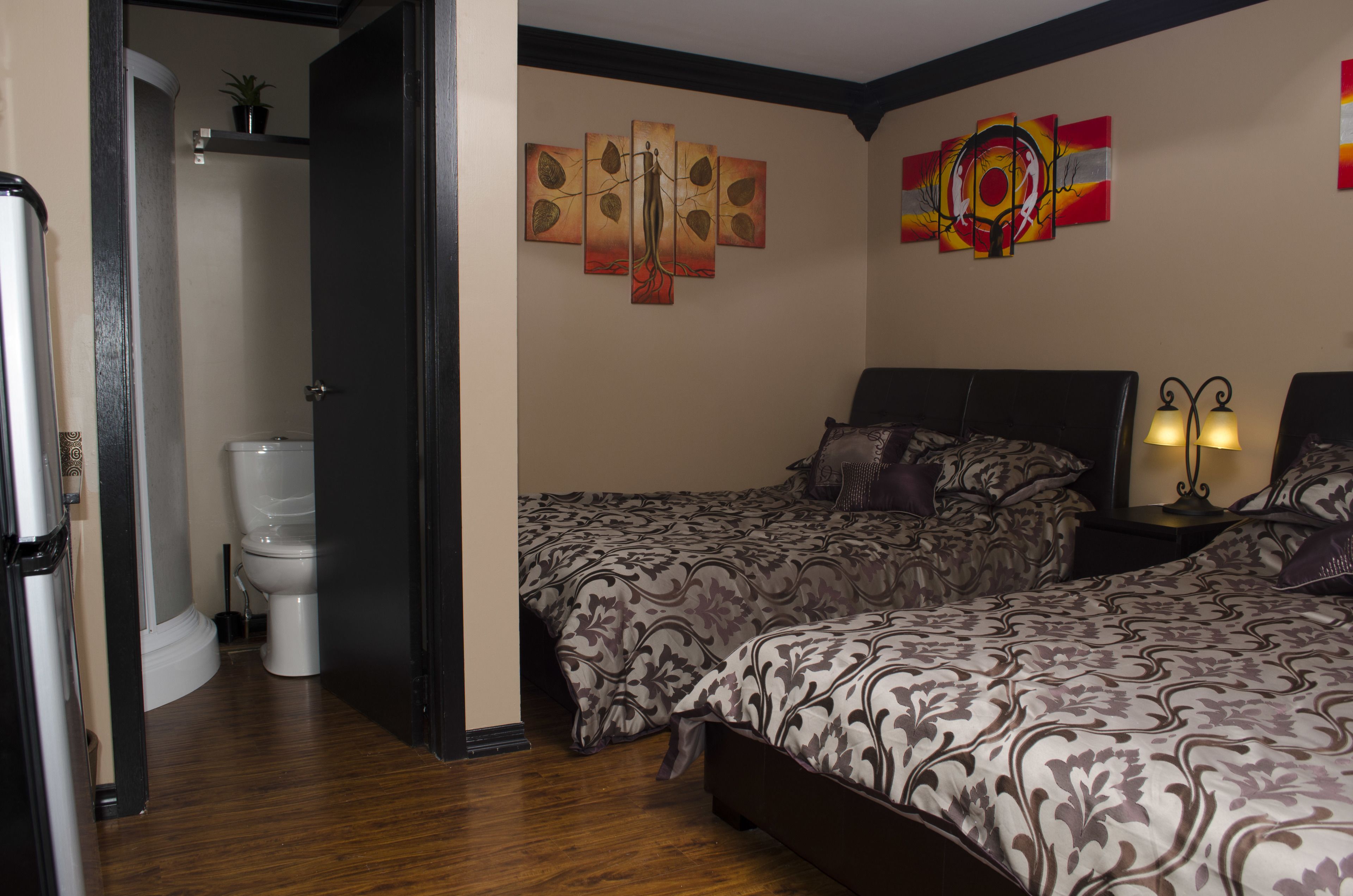 A hotel room with two beds, a bathroom with a toilet, and wall art.