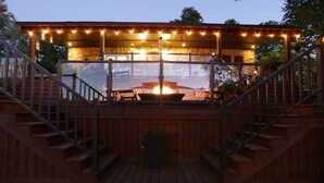 A wooden deck with a covered seating area, a fire pit, and a staircase leading to an upper level. - Footprints Resort (Hastings Highlands)