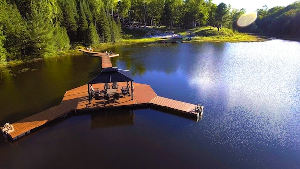 A wooden dock extending into a calm lake, with a covered seating area and chairs. - Footprints Resort (Hastings Highlands)