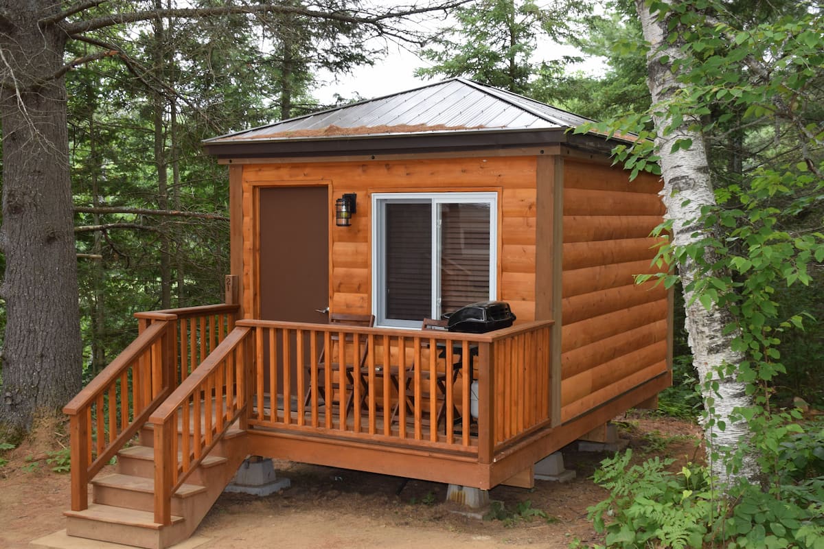 A wooden cabin with a deck, a door, and a window.
