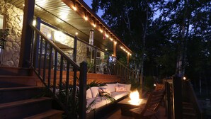 A wooden deck with a stone building, outdoor seating, and a staircase leading to a covered area. - Footprints Resort (Hastings Highlands)