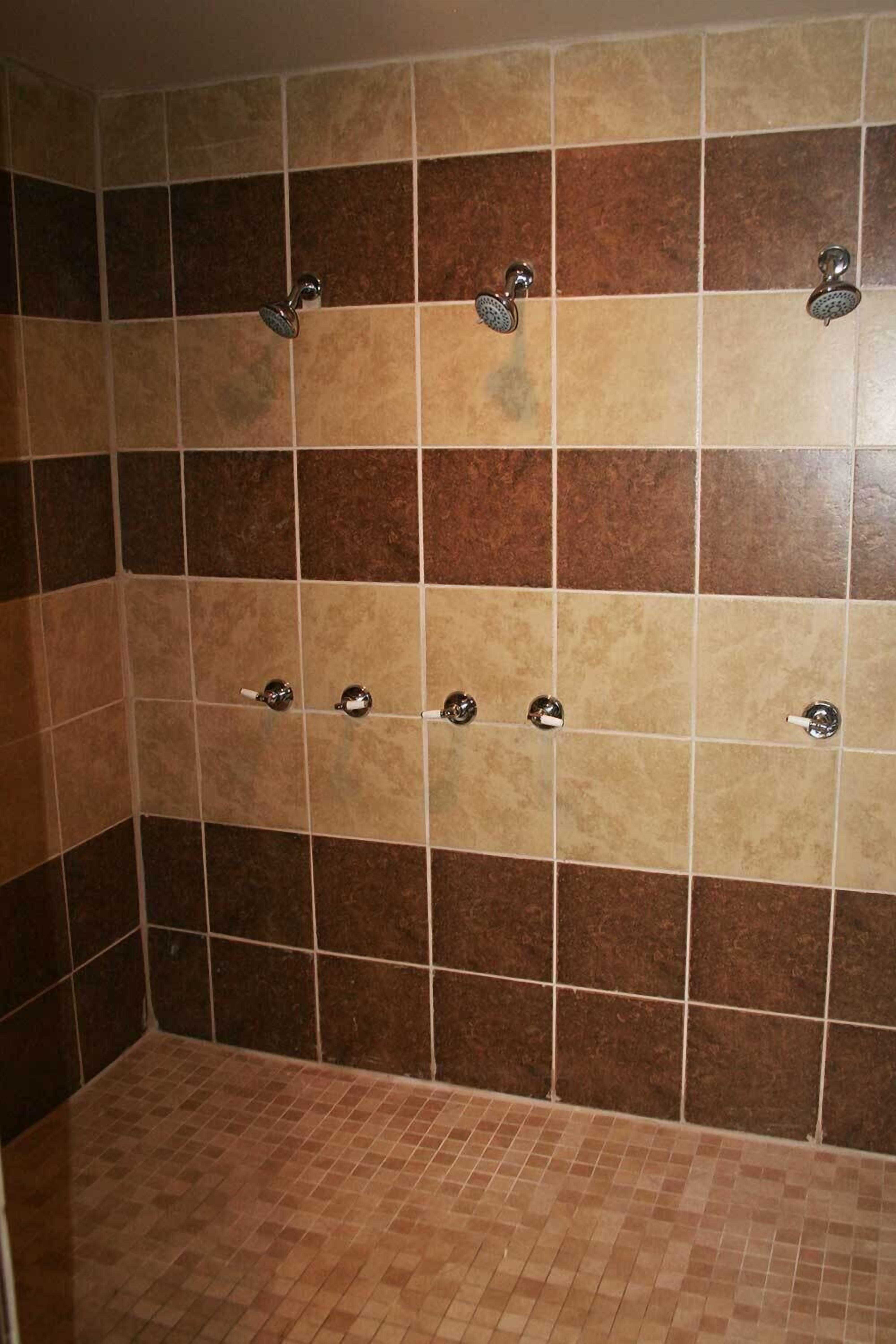 Área de duche com vários chuveiros e soalho em azulejo.