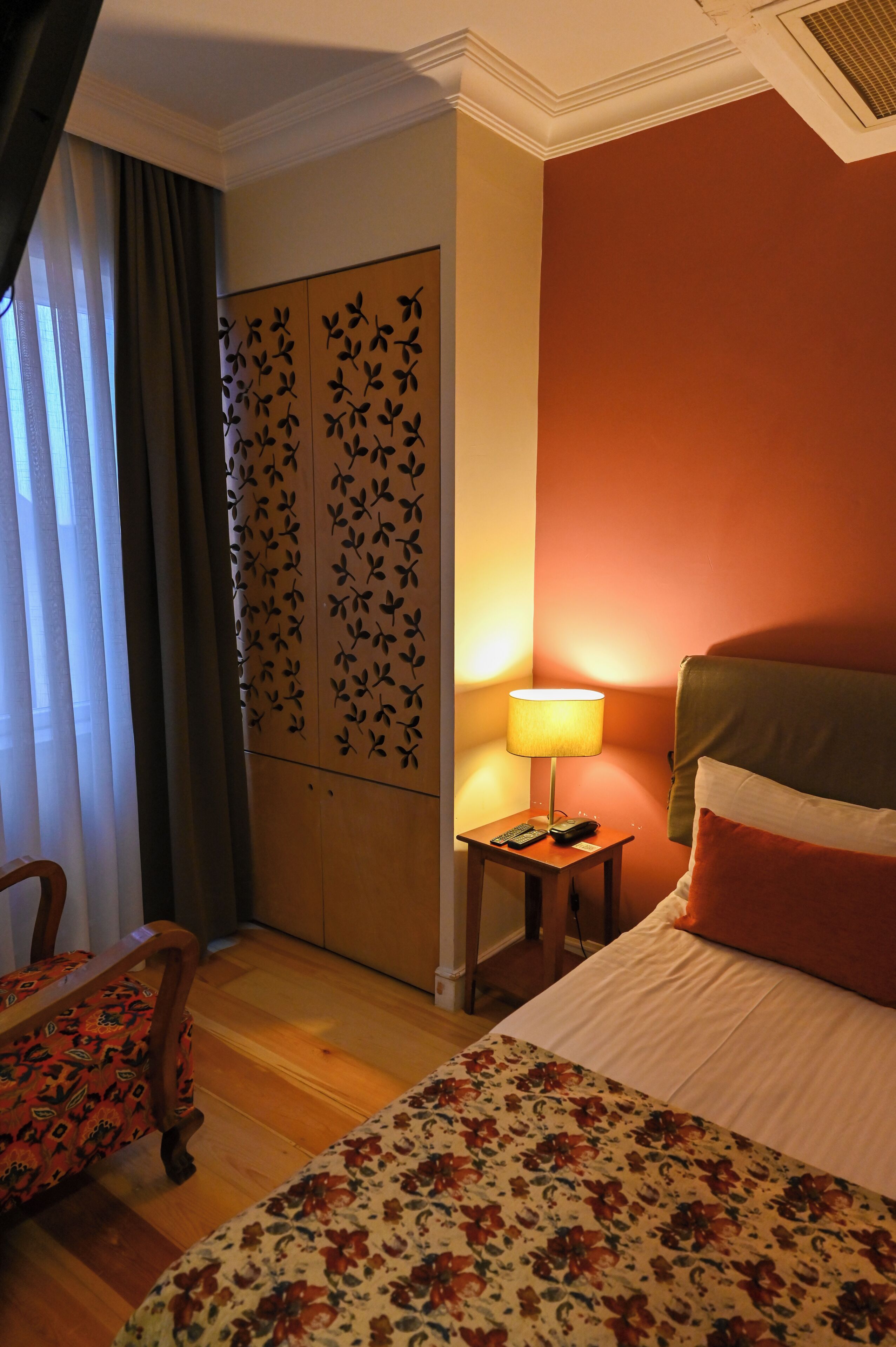 Ein Hotelzimmer mit Bett, Nachttisch mit Lampe, Sessel und Holzboden, sowie einer Dekorationstafel.