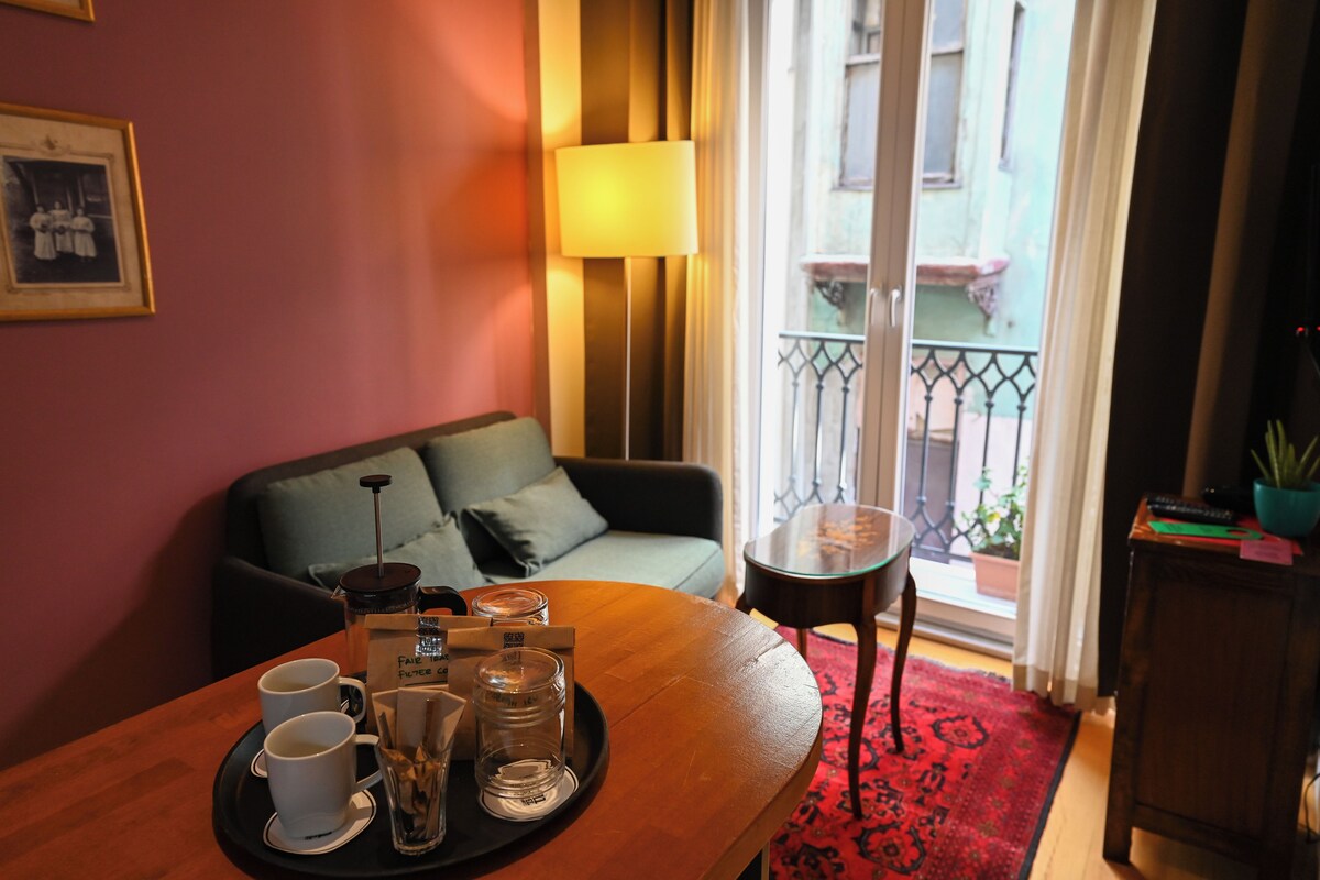 Quarto acolhedor com uma mesa de madeira posta para o café da manhã, um sofá, uma luminária e vista para a varanda.