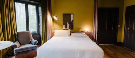 Una habitación de hotel con una cama grande, una silla, una mesita y una ventana con cortinas.