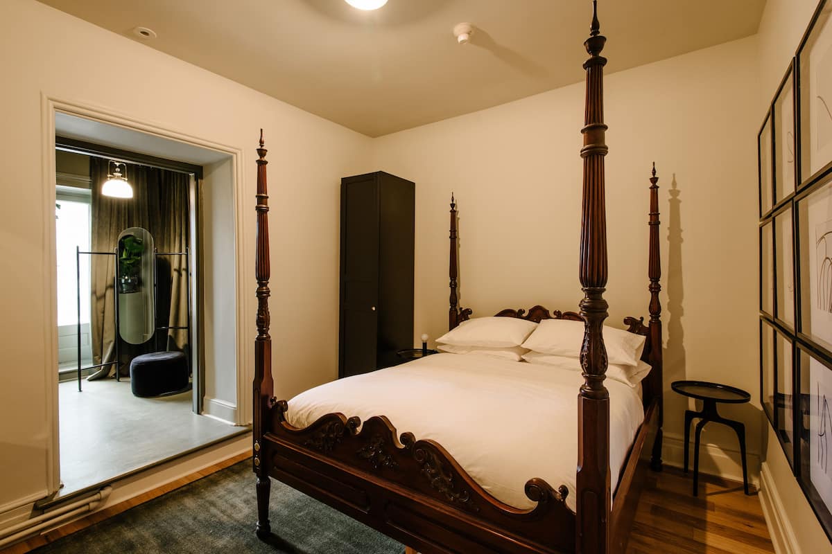 A four-poster bed in a bedroom with a wooden floor, a small round table, and a wardrobe.