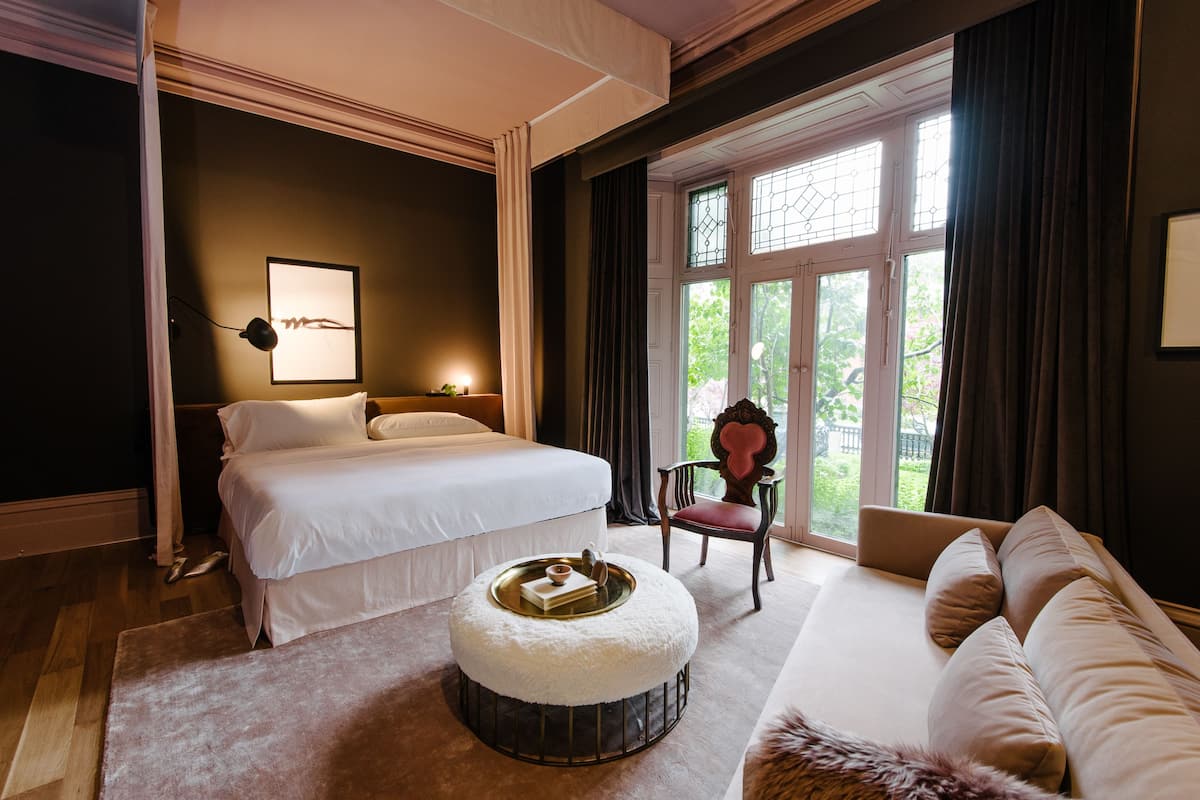 A bedroom with a bed, a chair, a sofa, and a window with curtains.