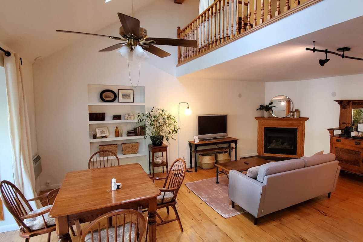 A spacious living room with a wooden dining table, a sofa, a television, and a fireplace.