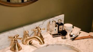 Een badkamer met een marmeren wastafel, gouden kranen en toiletartikelen.