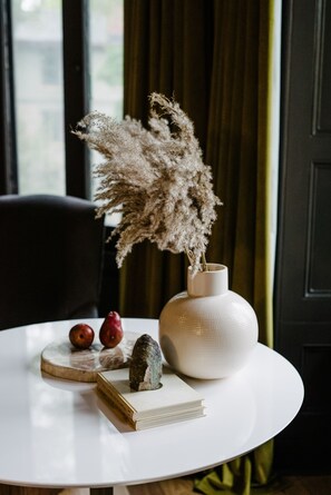 A round white table with a white vase containing dried pampas grass, a book, and two apples.