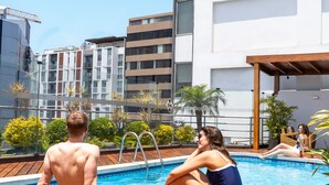 A rooftop pool area with a wooden deck, a lounge chair, and a view of modern buildings in the background. - Jose Antonio Executive (Lima)