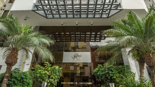 A modern hotel entrance with a geometric facade, palm trees, and a clear sky. - Jose Antonio Executive (Lima)