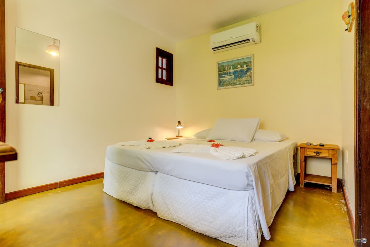 A neatly made bed with white linens and a small bedside table with a lamp.
