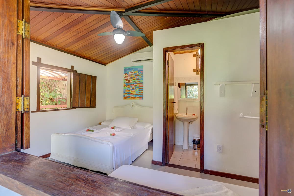 A bedroom with a bed, a wooden ceiling, a painting, a sink, and a door.