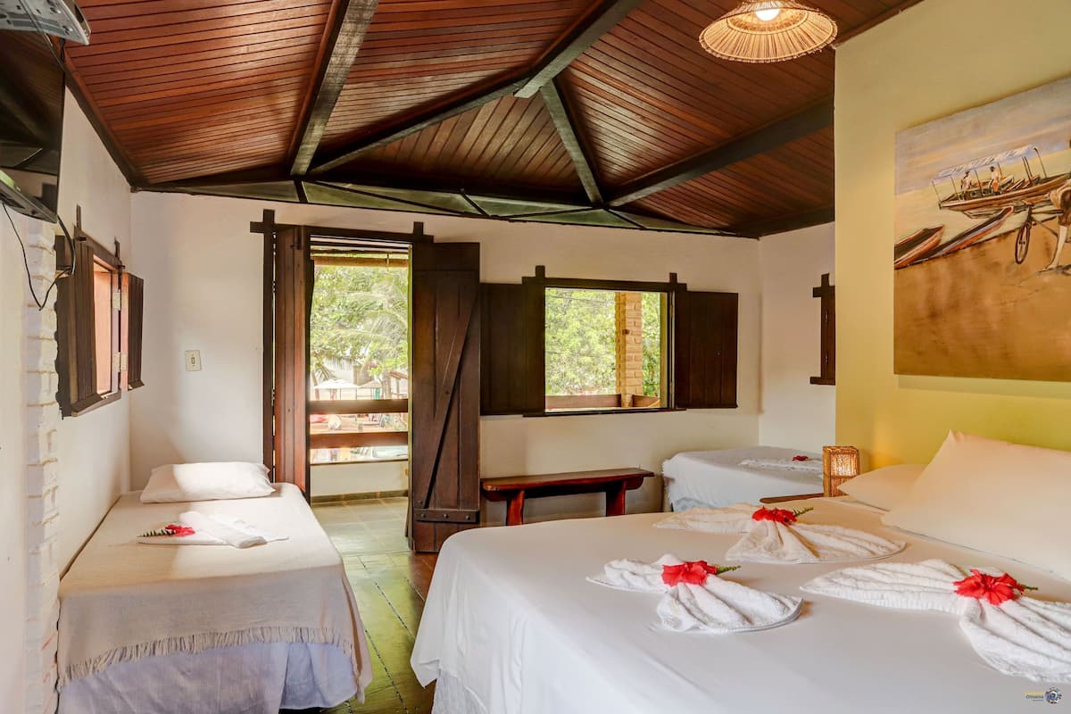 A room with two beds, a wooden ceiling, a window, and a painting on the wall.