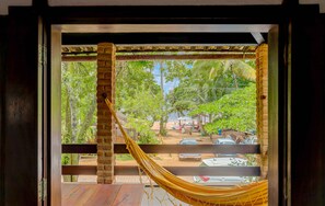 A hammock on a balcony with a view of a garden and parked cars. - Pousada Piratas (Itacaré)