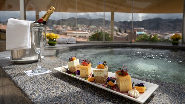 A table with a glass of champagne, a bottle of champagne, and a plate of desserts with fruit garnishes. - Jose Antonio Cusco Hotel (Cusco)