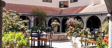 A courtyard with a stone archway, outdoor seating, and a building with multiple windows in the background.