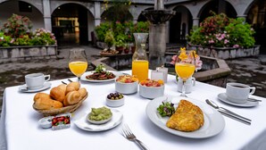 A breakfast table set with croissants, fruit, and coffee, overlooking a courtyard with a fountain and potted plants. - Jose Antonio Cusco Hotel (Cusco)