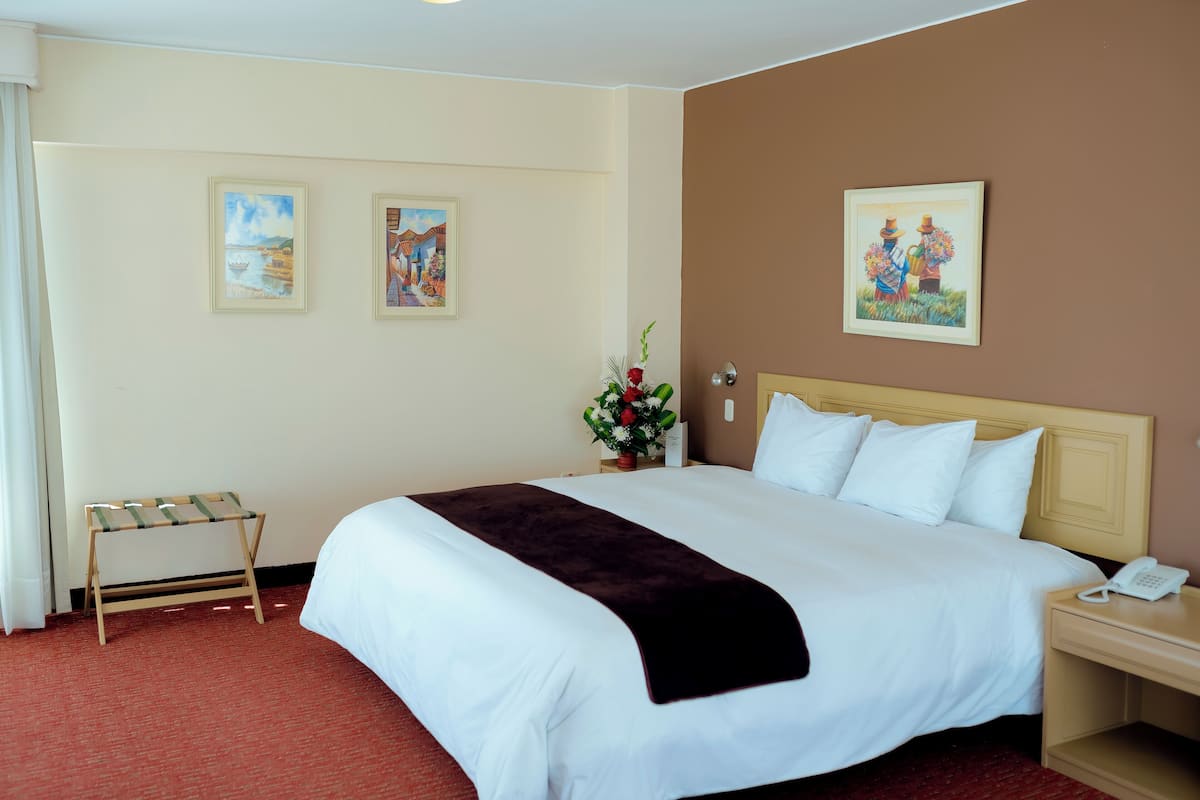 Une chambre d’hôtel avec un grand lit, une table de chevet avec un téléphone et deux tableaux encadrés au mur.