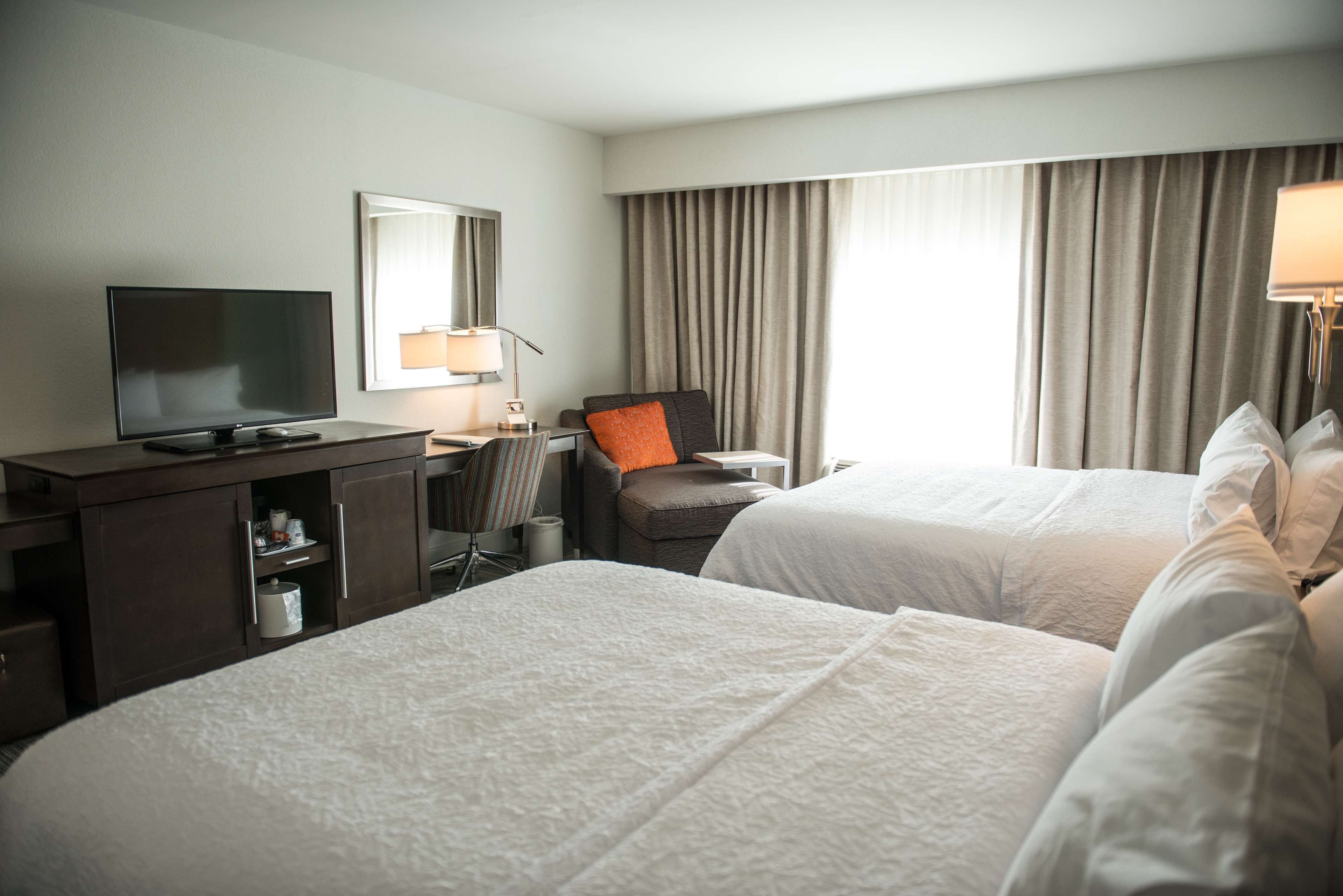 A hotel room with two beds, a desk with a television, a chair, and a lamp.